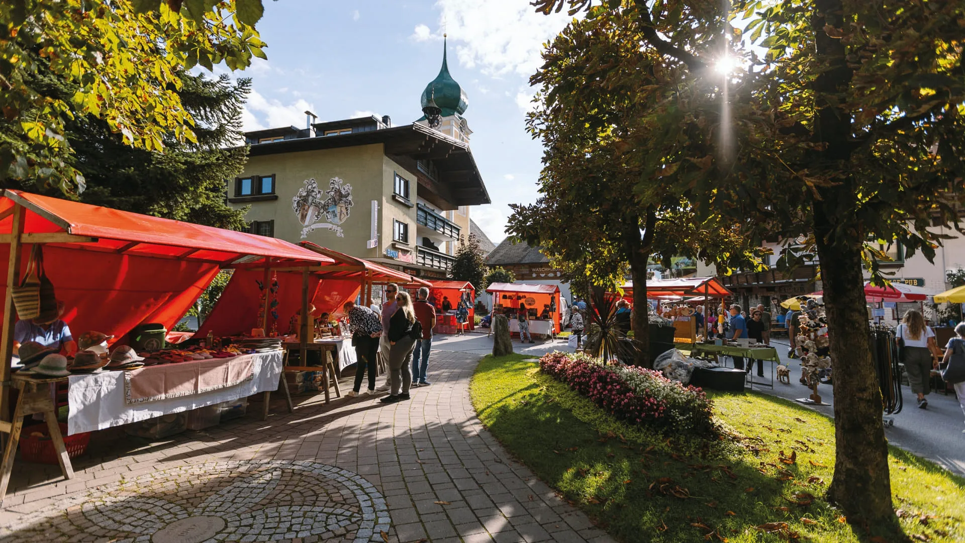 Markt mit roten Ständen und grünen Bäumen in Brixental im Sommer