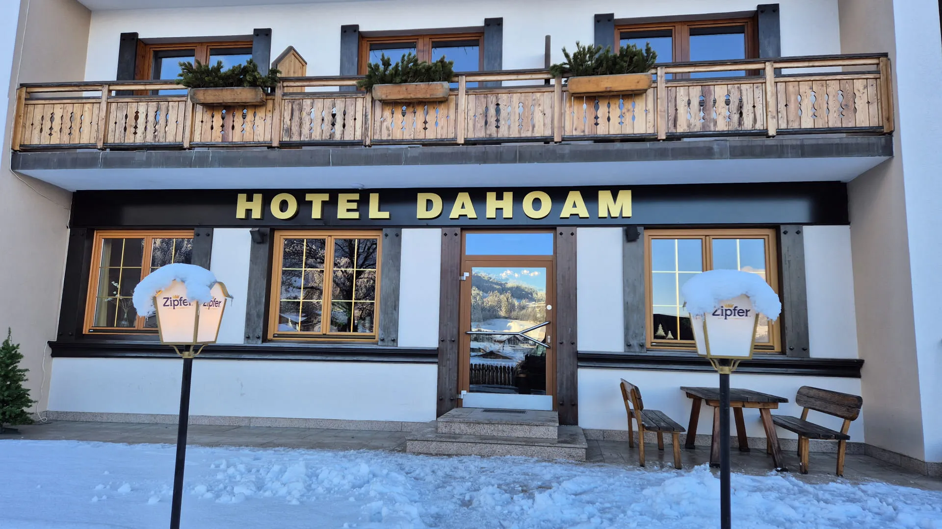 Hotel Dahoam mit Balkon und Sitzgelegenheit im Schnee.