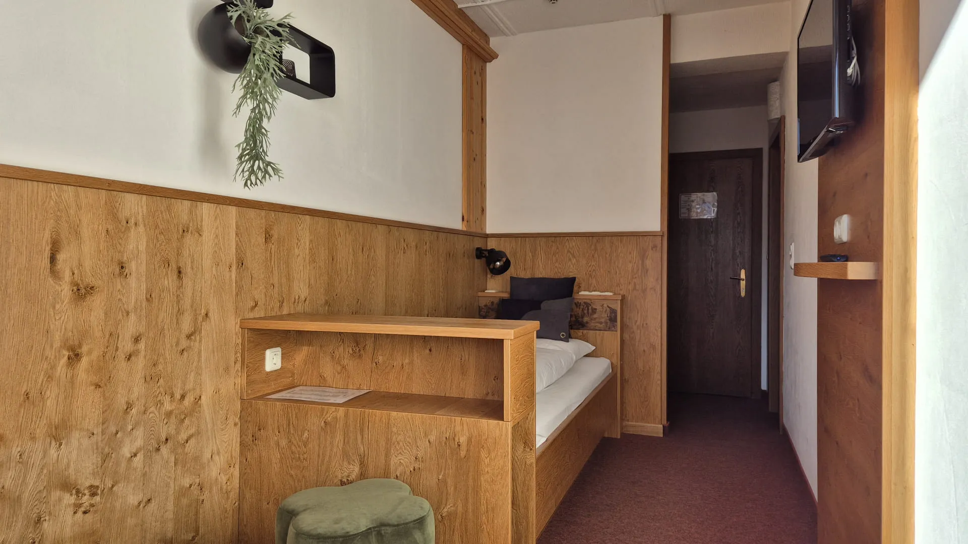 Heller Flur mit Holzverkleidung und Bett, Fernseher und Pflanze