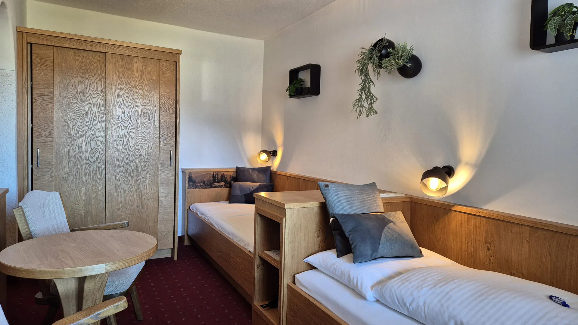 Ein Zweibettzimmer mit zwei Betten, einem kleinen Tisch und Wandpflanzen