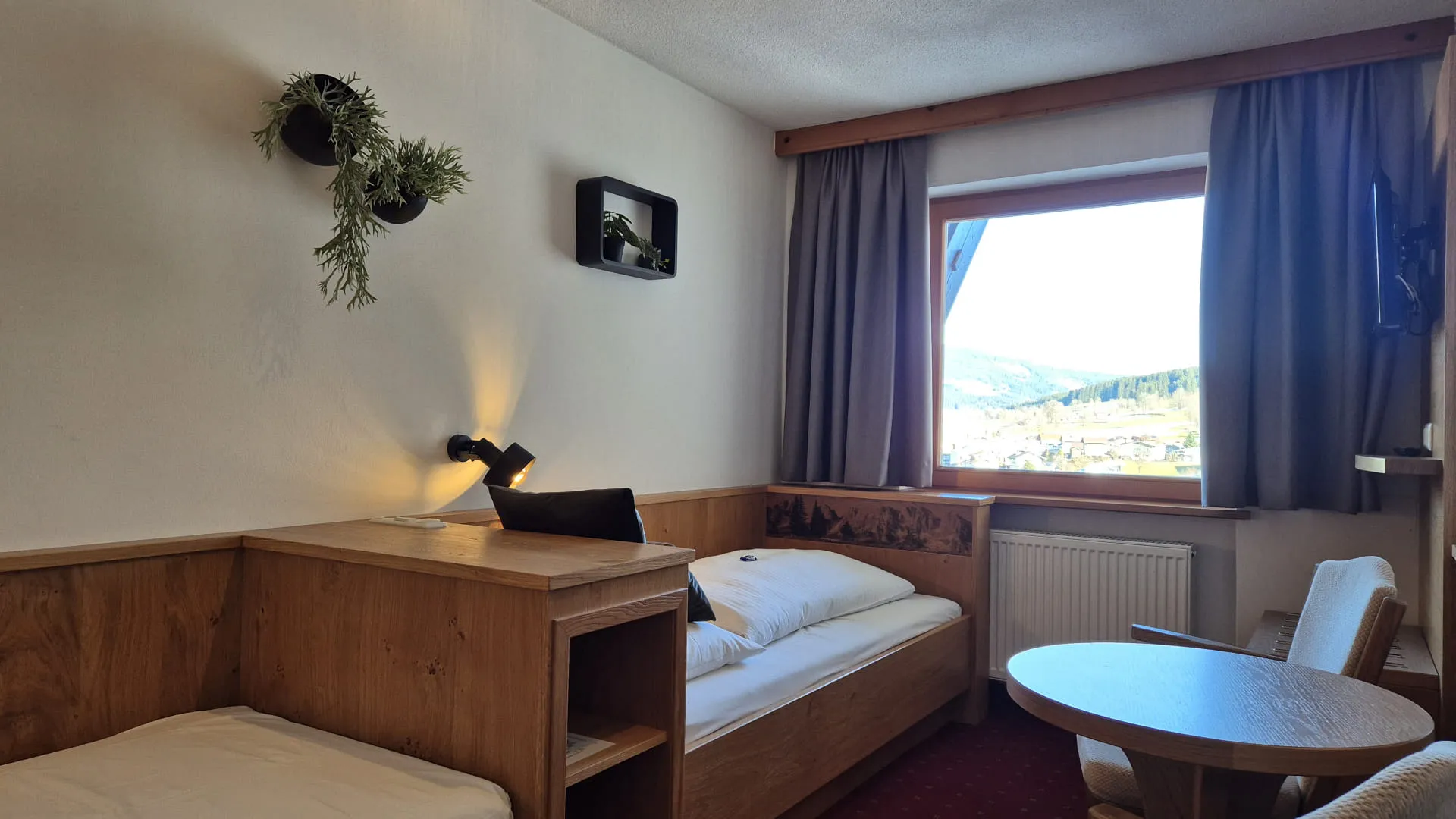 Ein gemütliches Zimmer mit zwei Betten, einem Tisch und einem großen Fenster mit Blick auf eine malerische Aussicht.